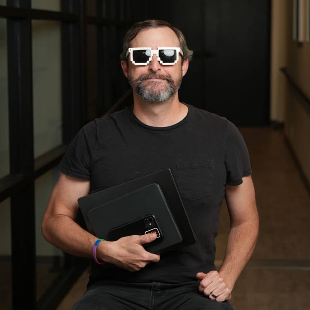 Matt Overwine sitting with sun glasses, a laptop, tablet, and mobile phone.